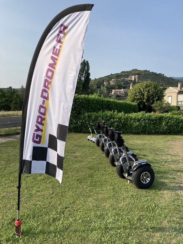 Photo des gyropodes avec un drapeau gyro-drome.fr devant le village de Montbrun-les-Bains